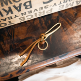 Brass fishhook keychain with brown leather on tabletop