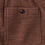 Close up of dark button-secured back pocket on a pair of burgundy textured pants