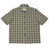 Front of short sleeved button up shirt in a green and brown plaid fabric with a row of small dark buttons going down the center. 